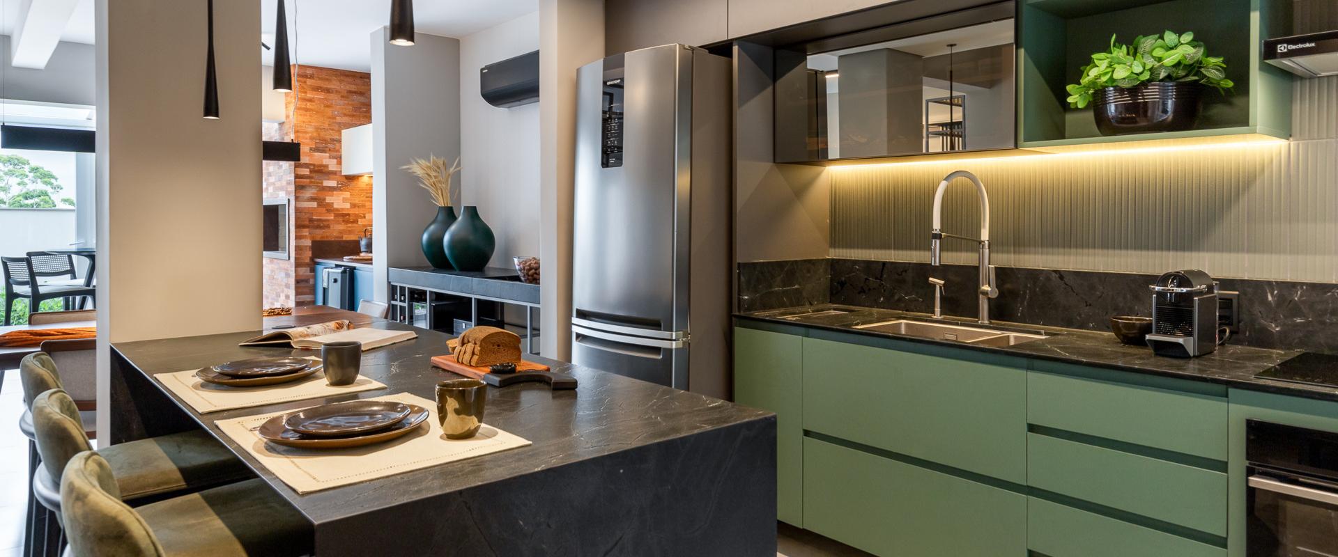 Cozinha planejada com ilha em granito preto, marcenaria verde-oliva e cooktop integrado, projeto de arquitetura de interiores residencial