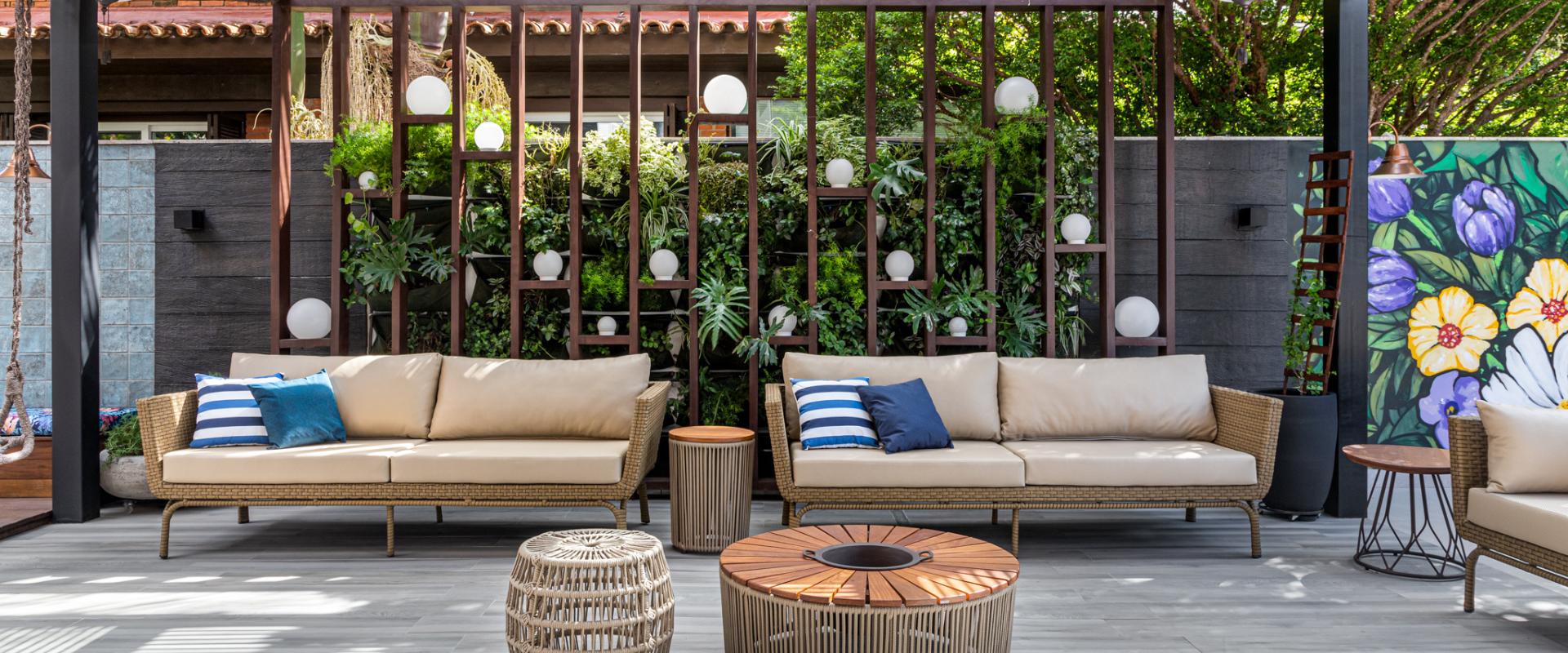Área de estar externa com sofás em fibra sintética, almofadas azuis, jardim vertical e iluminação em esferas, projeto de arquitetura de interiores ao ar livre